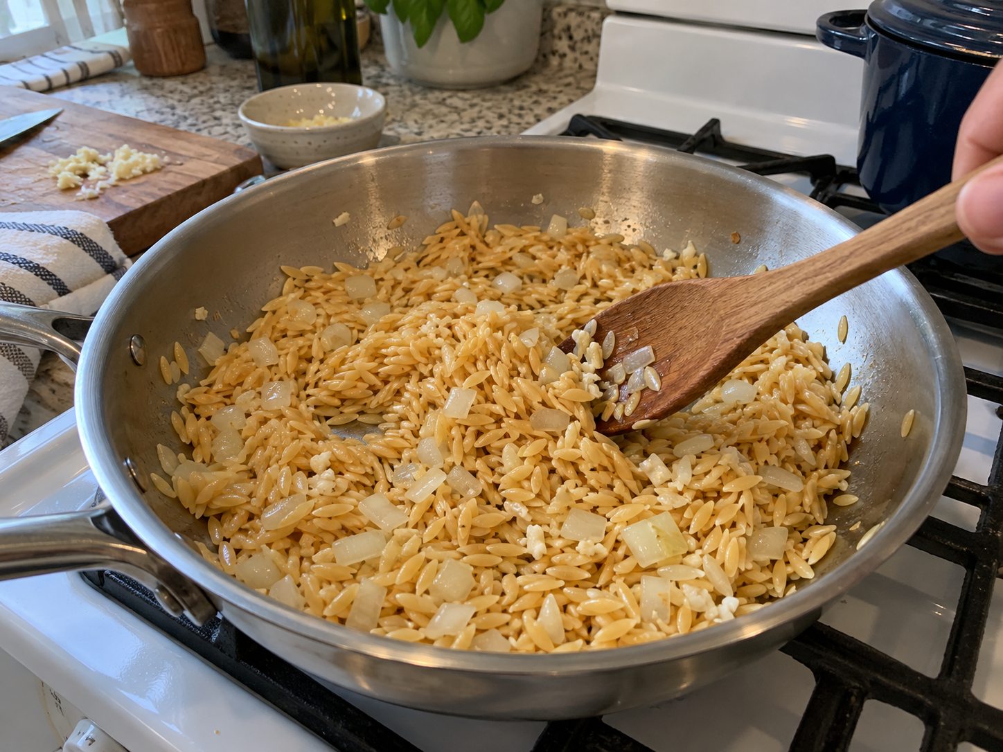 Dry orzo stirred with sautéed onion and garlic in a skillet
